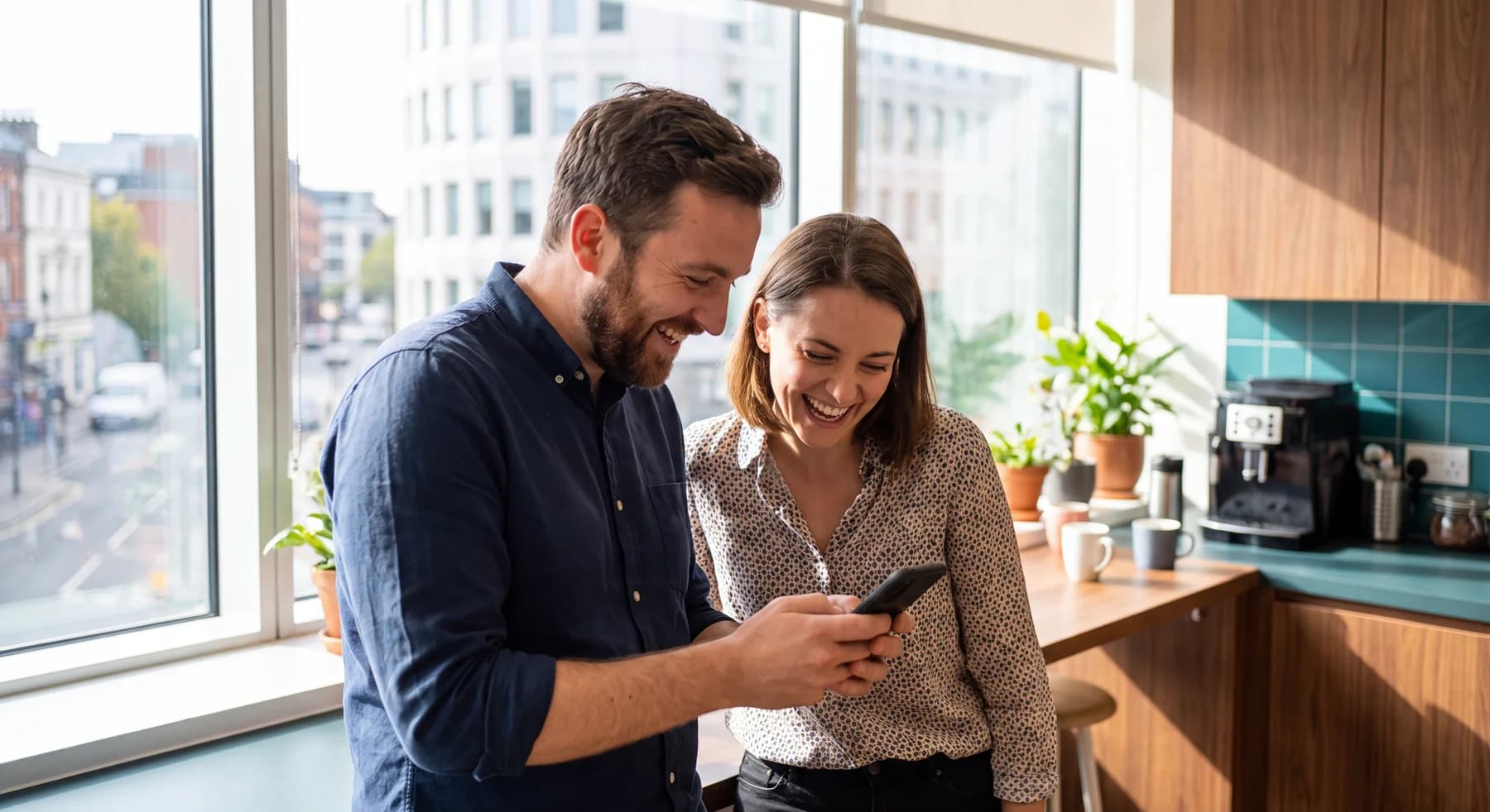 Deux salariés sourient devant un téléphone à la pause café
